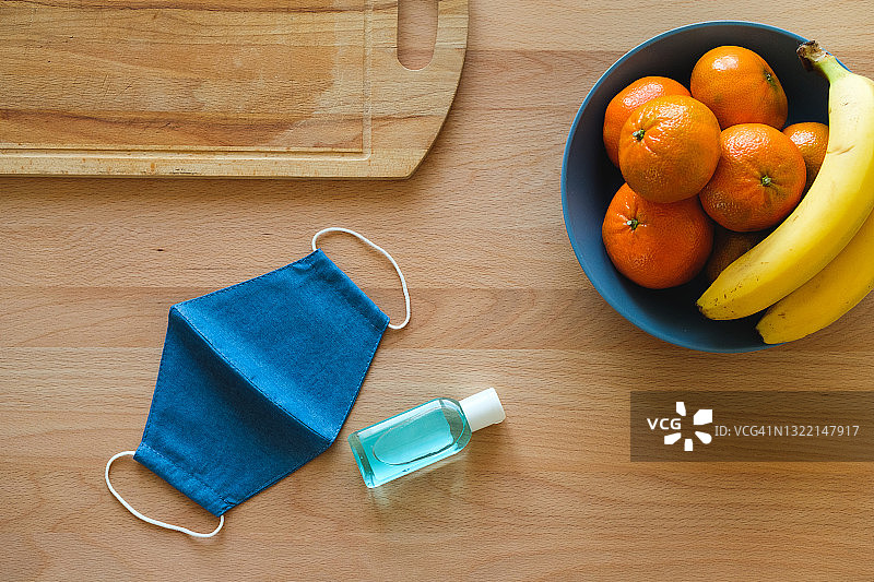 医用防护口罩、免洗洗手液、水果，木质厨房桌上的橘子和香蕉，素食主义、纯素食主义和生食，预防新冠病毒传播，疫情隔离生活图片素材