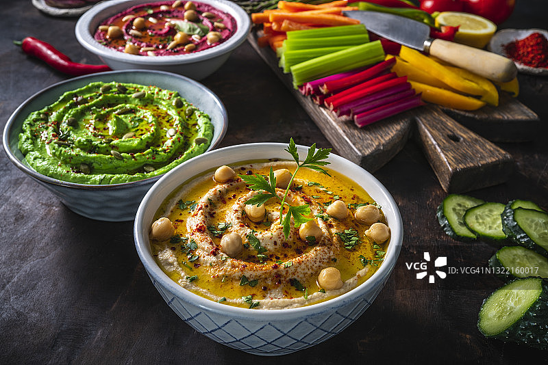 三碗鹰嘴豆，鳄梨，甜菜根和切好的蔬菜蘸在深色的木头上图片素材