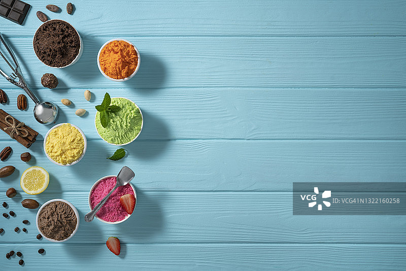 蓝色木板上各种口味的什锦冰淇淋杯和蛋卷图片素材