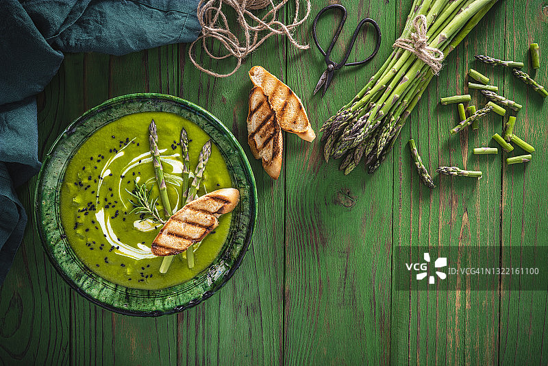 芦笋汤盘配食材和烤面包片，置于绿色木板上图片素材