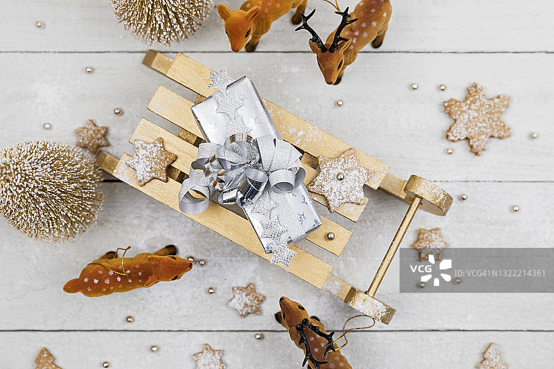玩具雪橇上的圣诞礼物，周围是玩具鹿和白色木制背景下的自制饼干图片素材