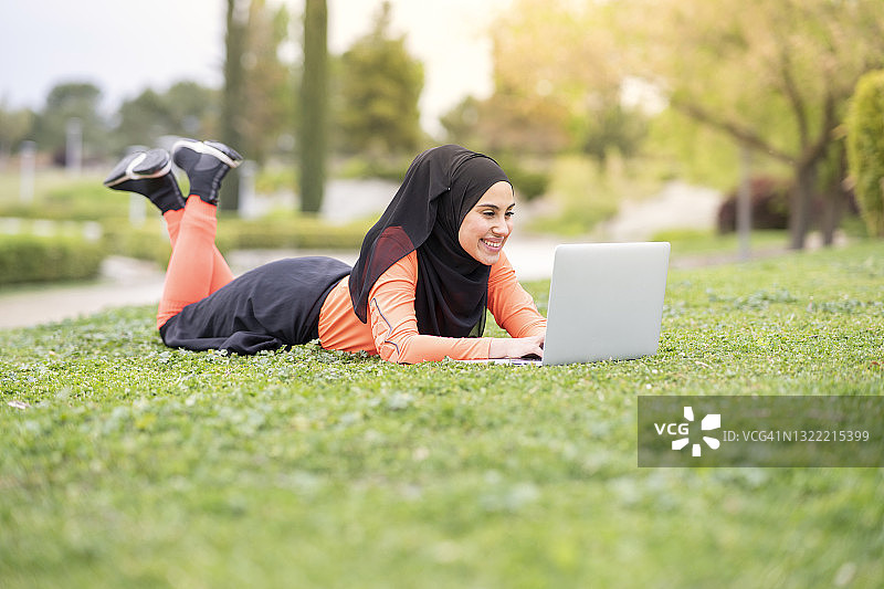 在公园里躺着使用笔记本电脑的微笑女人图片素材