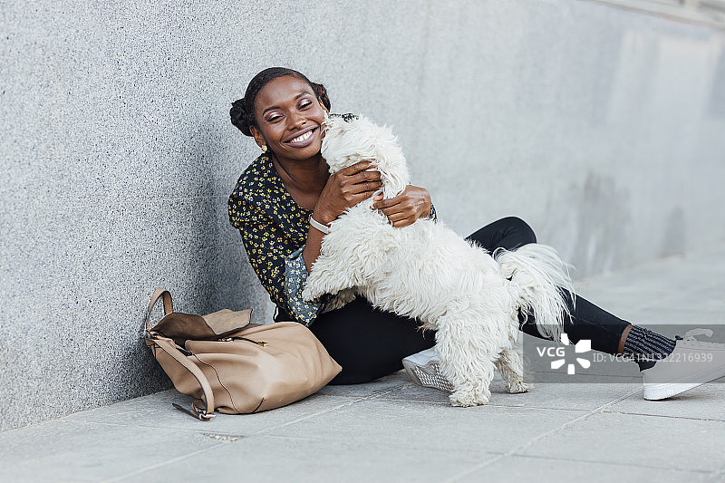 微笑的女人坐在人行道上和狗玩耍图片素材
