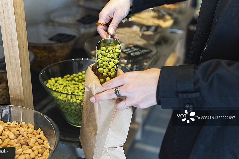 女人在商店将青豆放入纸袋中图片素材