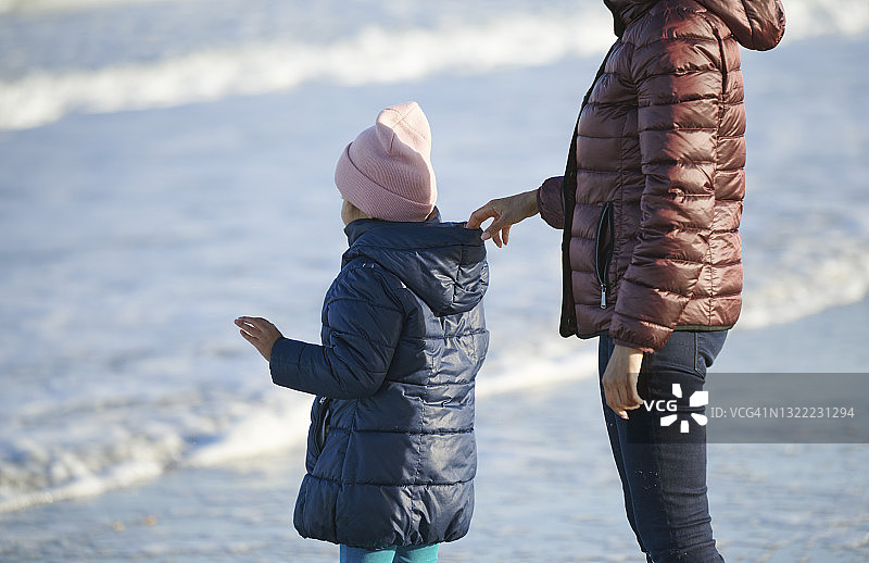 细心的女人在海滩上扶着戴兜帽的女儿图片素材