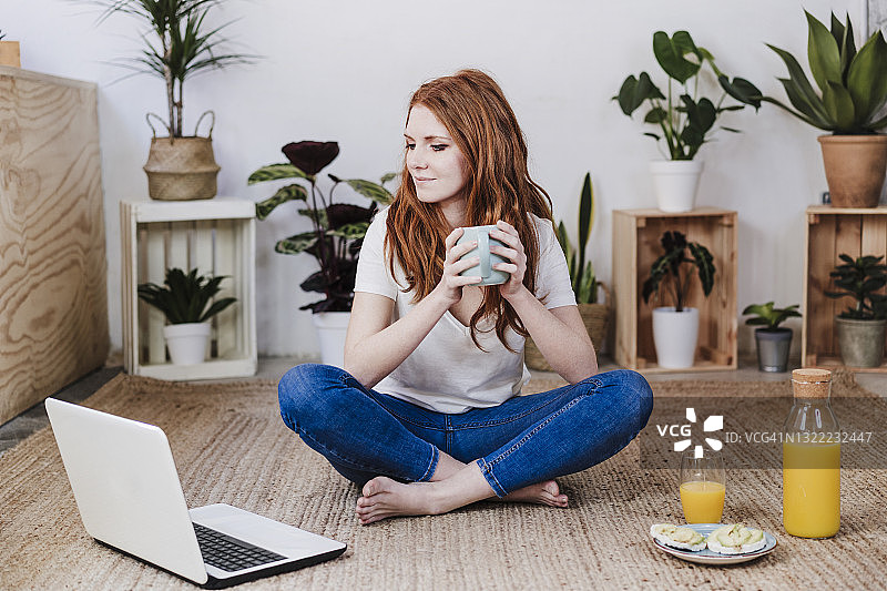 在家中地板上喝咖啡看笔记本电脑的女人图片素材