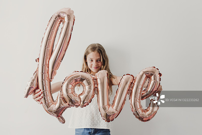 微笑女孩站在墙前，展示爱心气球图片素材