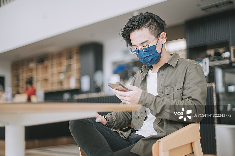 戴着防护口罩在咖啡馆刷社交媒体的亚洲青少年图片素材