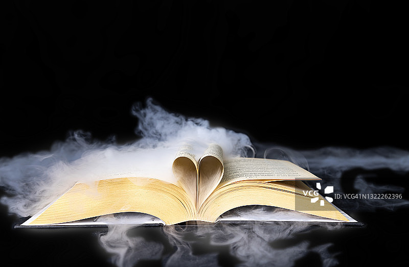 打开的书本，烟雾效果流过书页，穿过黑色背景上书页组成的心形图片素材