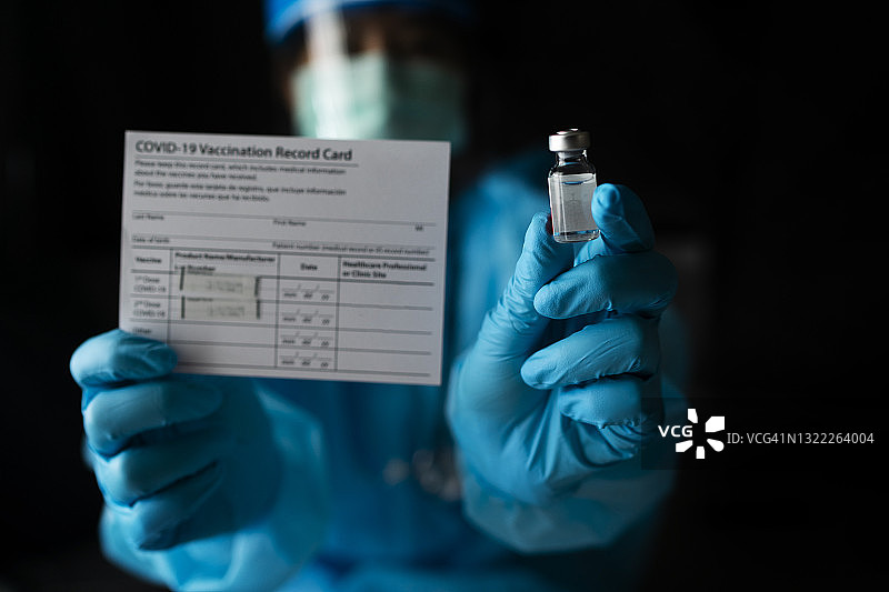 医生戴着外科手套，准备新冠疫苗（2019-nCoV），手持疫苗接种护照或接种卡图片素材