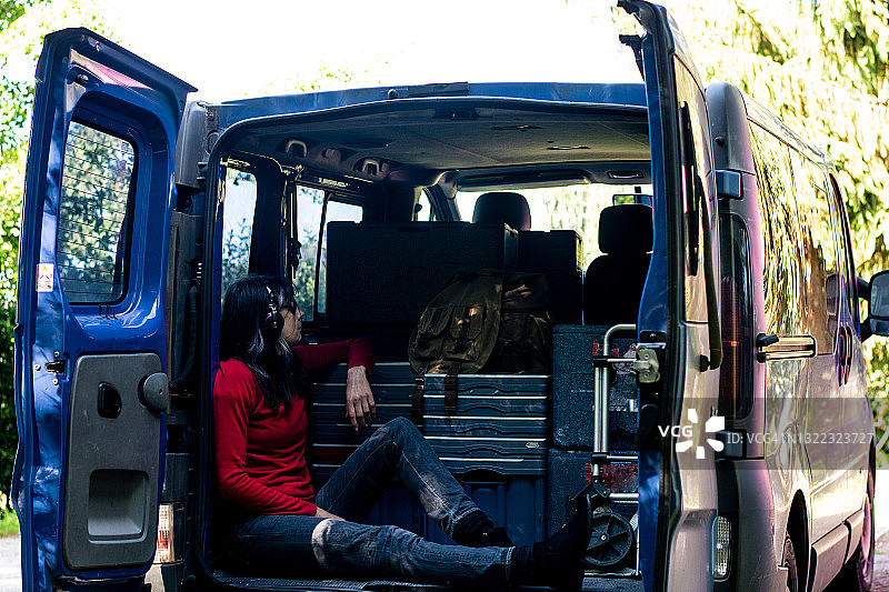 坐在蓝色货车后备箱里，放松听音乐的女人图片素材