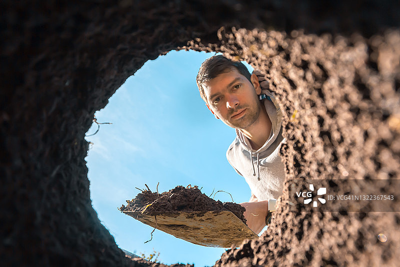 男人惊讶地看着脏土和被挖掘的洞，寻找宝藏图片素材