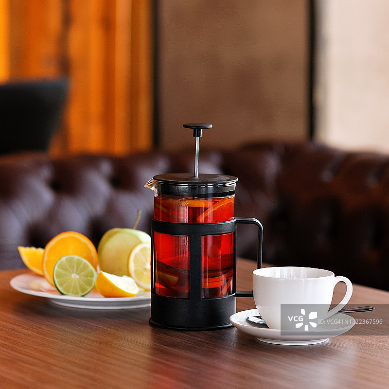 冲泡好的红茶，木桌上的茶壶或法式滤压壶，配有茶杯和柑橘水果盘，虚化背景留有复制空间，柔焦图片素材