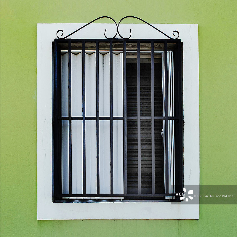 绿色墙壁上带有装饰性锻铁安全栏的窗户图片素材