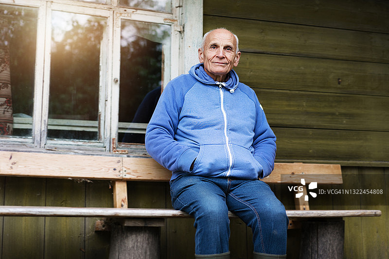 孤独的灰发老人在房屋墙边的木凳上图片素材