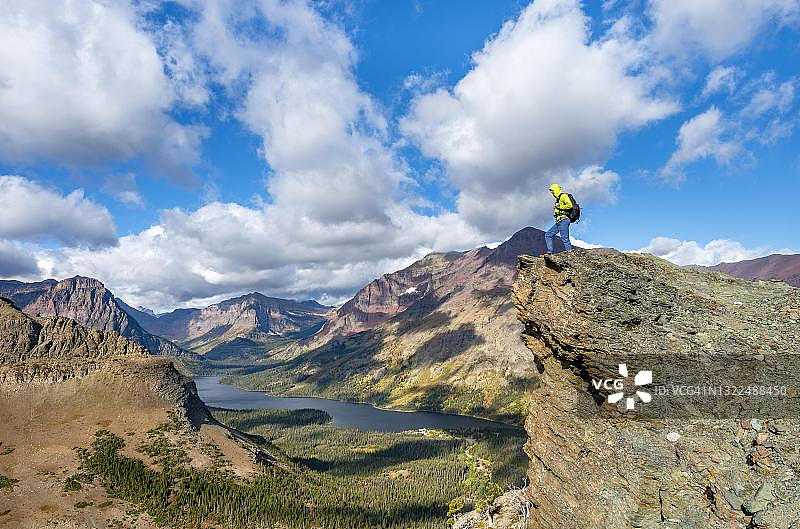 徒步者站在岩石上，眺望美国蒙大拿州冰川国家公园的两药湖、狼升山和西诺帕山的山峰，以及通往风景点的徒步小径图片素材