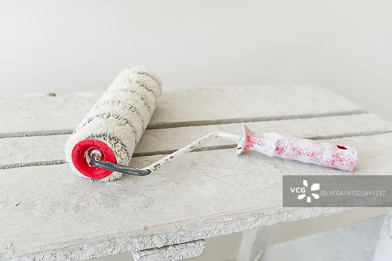 木桌或梯子上沾满白色油漆的建筑滚筒，房屋建造或公寓维修工具图片素材