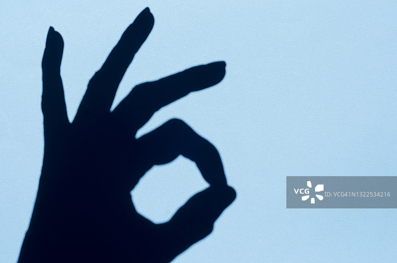 人手在柔和的蓝色背景上做出OK手势图片素材