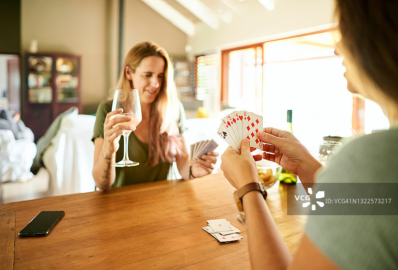 微笑的女性朋友在家玩纸牌和喝葡萄酒图片素材