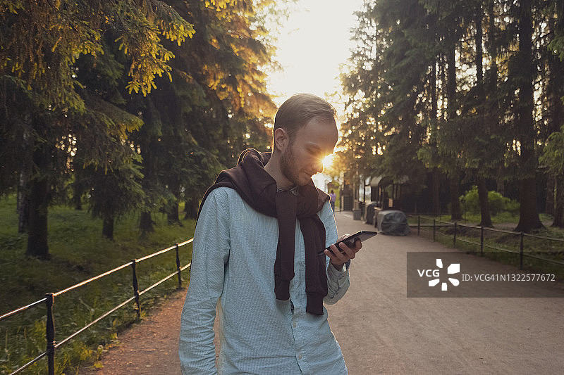 年轻商人在公园散步时使用手机图片素材
