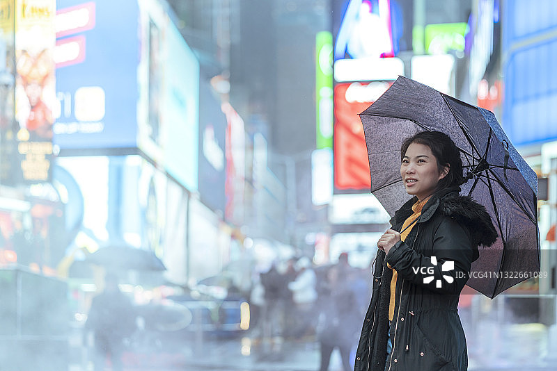 在纽约时代广场雨中撑伞的亚洲女游客图片素材