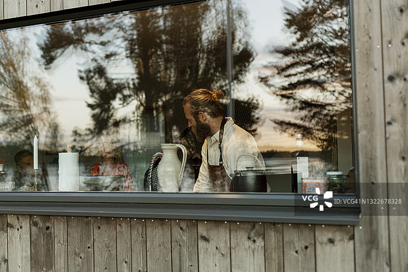 透过窗户看到的在厨房里穿着围裙的男人图片素材