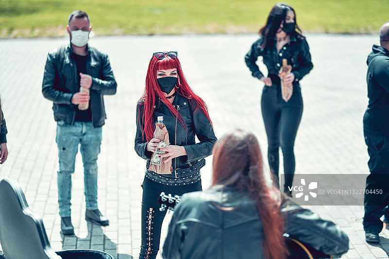 哥特风红发女子欣赏街头艺人表演并向吉他盒里投钱图片素材