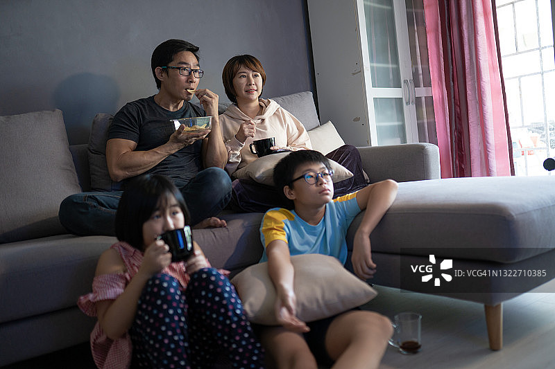 亚洲家庭坐在沙发上一起在家看电视图片素材