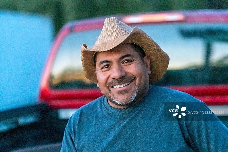 微笑的西班牙裔农场工戴着牛仔帽看着镜头图片素材