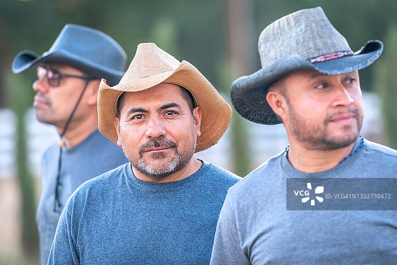 三名戴着牛仔帽的西班牙裔成熟农业男工看着镜头微笑图片素材