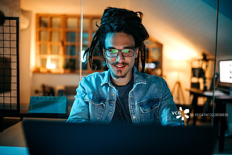 快乐的帅气年轻人在他的小型家庭办公室里使用电脑图片素材