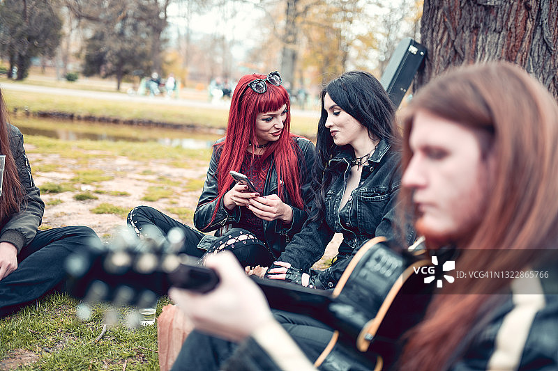 在公园里与男友闲逛并浏览社交媒体的重金属摇滚女图片素材