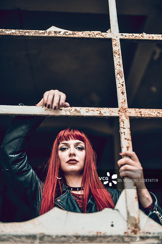 红发哥特风女子在废弃建筑中透过生锈的窗户看图片素材