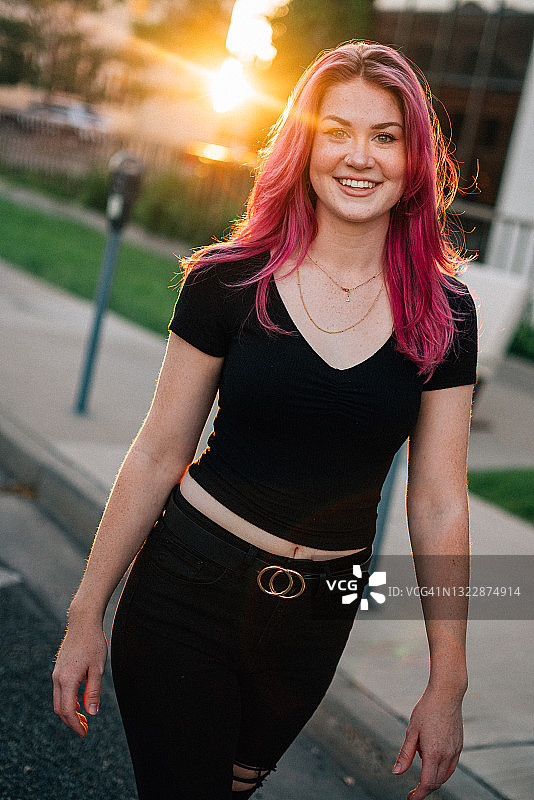在夏天户外，一位留着亮粉色染发的时髦快乐年轻女子在阳光下行走图片素材