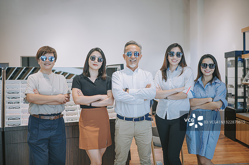 华人男女手臂交叉，戴着太阳镜，在眼镜店前对着镜头微笑图片素材
