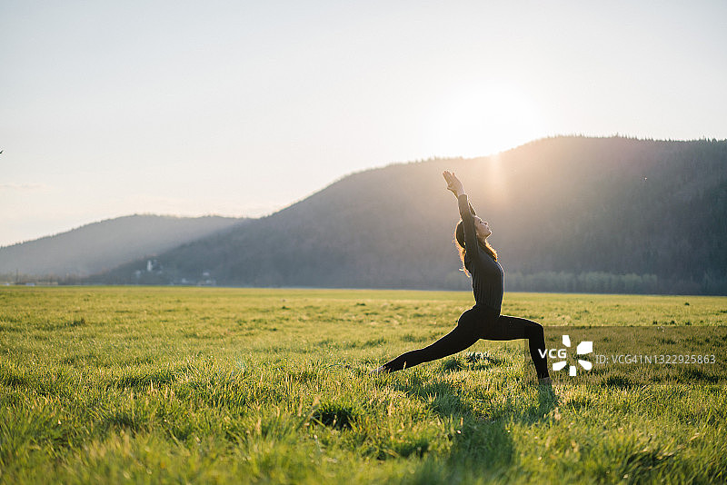 年轻女人在日出时分的草地上练习瑜伽图片素材