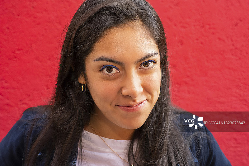 年轻的拉丁裔女子扬起眉毛看着镜头，红色背景图片素材