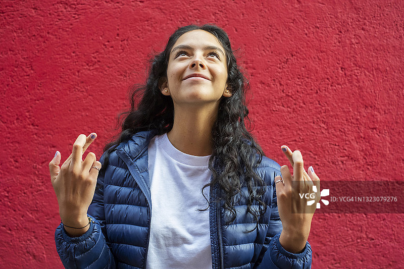 抬头，手指交叉，充满希望和祈祷的年轻拉丁裔女子，红色背景图片素材