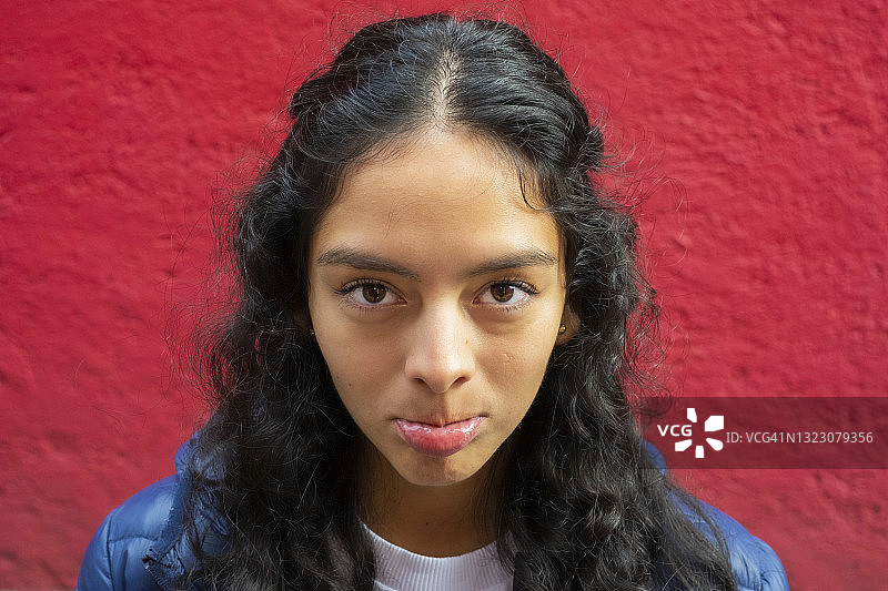 失望地看着镜头，撅着嘴，像个孩子一样要哭的年轻拉丁裔女子，红色背景图片素材