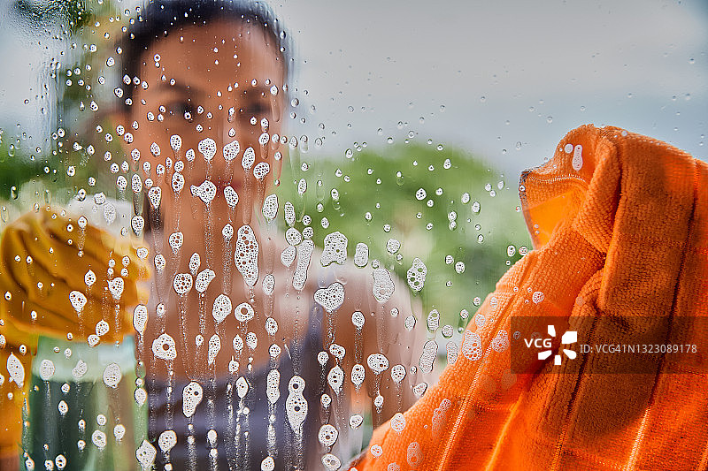 戴着防护手套，在家用抹布和清洁剂清洁窗户的拉美裔年轻女子图片素材