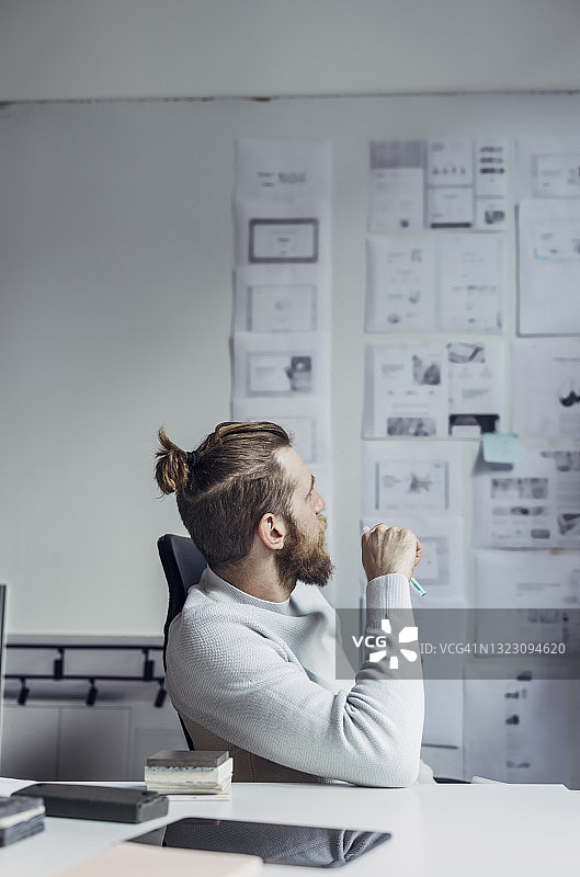 坐在办公桌前，看着图板上项目的帅气年轻建筑师图片素材