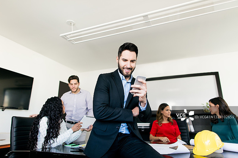 年轻男建筑师在会议室使用手机并微笑图片素材