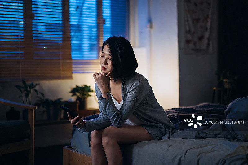 睡前在床上使用智能手机的年轻亚洲女人图片素材