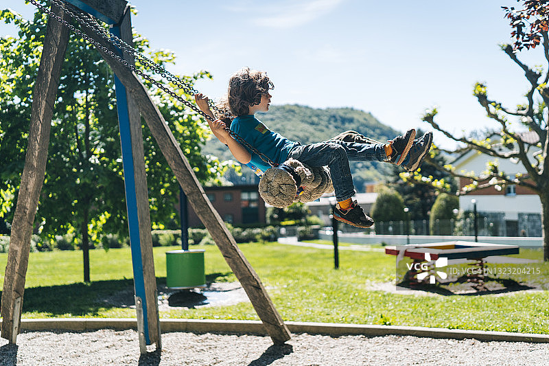 母亲在操场上推着秋千上的小男孩图片素材