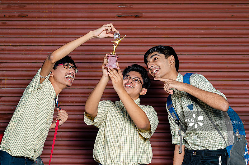 三个年轻学生享受胜利并举起奖杯的合影图片素材