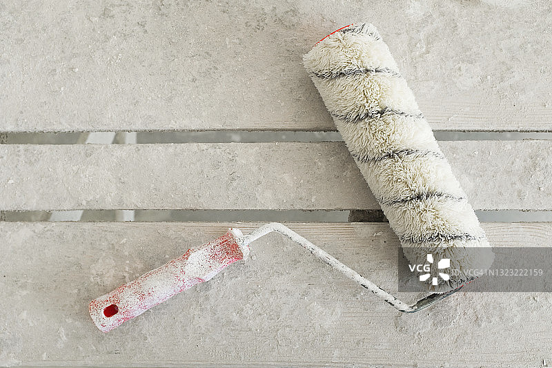 木桌或梯子上沾满白色油漆的建筑滚筒，房屋建造或公寓维修工具图片素材