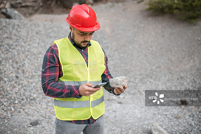 身穿制服，手持石头和手机的络腮胡工人图片素材