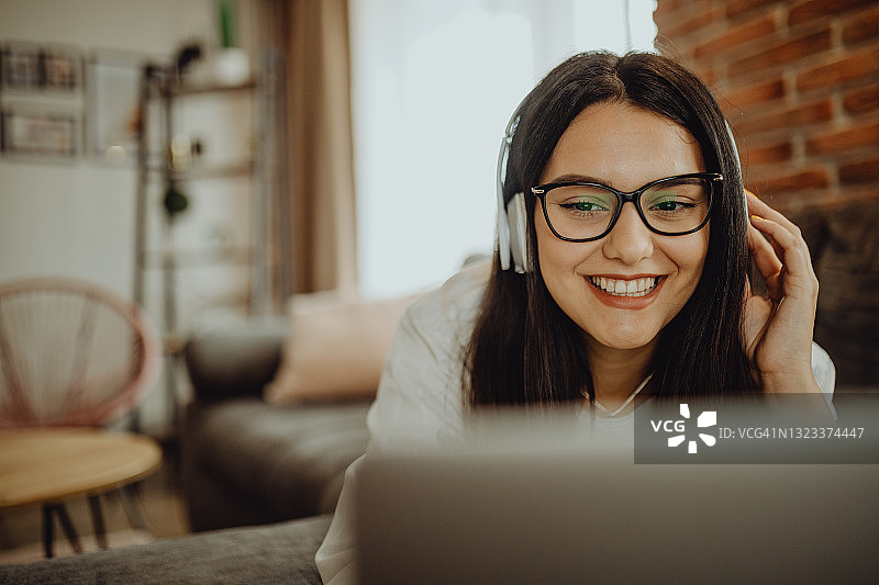 坐在沙发上用笔记本电脑耳机学习的年轻女学生图片素材