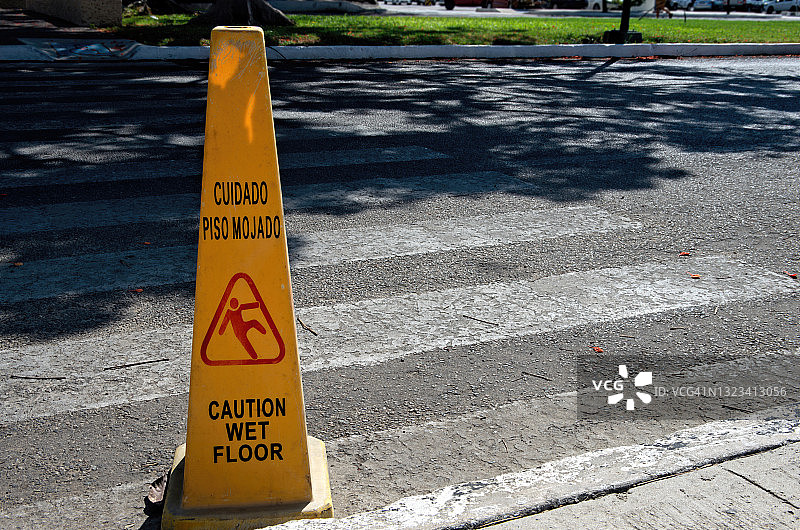 道路人行横道上的双语西班牙语和英语“小心地滑”独立式便携塑料警告标志图片素材