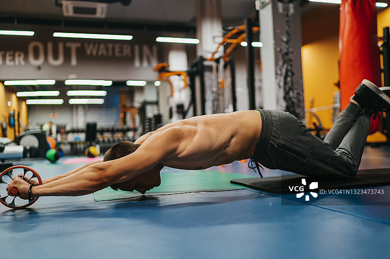 在健身房用健身轮锻炼的英俊男人图片素材